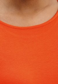 Tissu orange à côtes avec une texture lisse et un col rond. Le vêtement a une coupe ajustée, mettant en avant la simplicité du design.