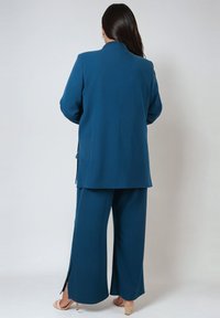 Teal tailored suit featuring a long blazer and wide-leg trousers. Soft fabric, smooth texture, side slits on trousers, and minimalist design.