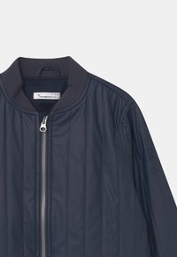 Navy quilted bomber jacket with a ribbed collar, featuring a front zipper and embossed logo detail on the sleeve. Smooth, lightweight material.