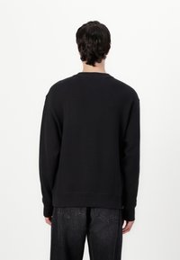 Sort sweatshirts lavet af struktureret stof, med rund halsudskæring, sænket skuldersøm og ribstrikkede manchetter. Bæres med mørke jeans.