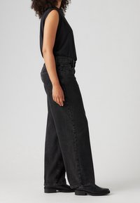 Svarta vida jeans i denim, med hög midja och avslappnad passform. Kombinerat med en svart ärmlös topp och svarta ankelboots.