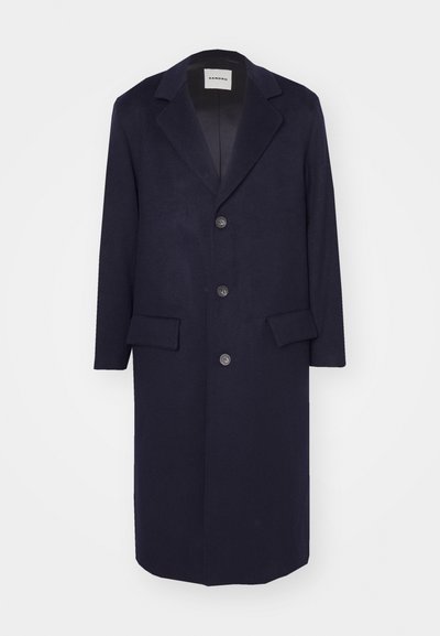 Cappotto di lana blu navy con design su misura, revers a punta, quattro bottoni e due tasche frontali. Texture liscia, lunghezza al ginocchio.