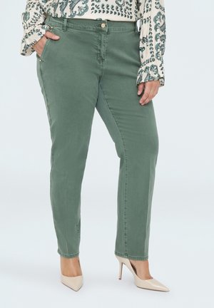Femme portant un pantalon vert droit, des talons hauts beige et un chemisier crème à manches longues avec des motifs cachemire verts.