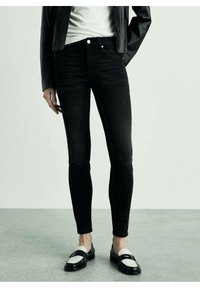 Vaqueros pitillo negros con una textura de denim suave, que cuentan con cintura alta, diseño de cinco bolsillos y costuras acentuadas. Combinados con mocasines en negro y blanco.