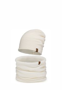 Kremowa dzianinowa czapka beanie i dopasowany ocieplacz na szyję. Oba mają miękką teksturę i posiadają małą brązową metkę marki.