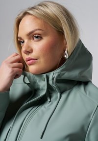 Mintgroene waterdichte jas met een hoge kraag, verstelbare koordjes en een rits aan de voorkant. Gladde textuur, met zilveren accenten.