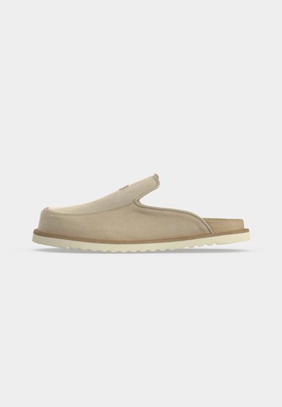 Sandale beige à enfiler avec bout fermé, talon ouvert, dessus en suédine souple et semelle en caoutchouc blanche texturée, montrée de profil sur fond blanc.