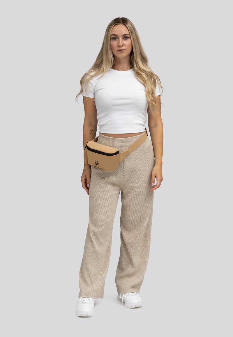 Beige heuptas met zwarte accenten, gedragen over een witte top en licht beige wijde broek. Zachte textuur, minimalistisch ontwerp.