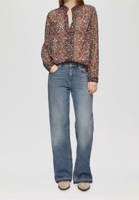 Blouse noire à motifs floraux avec manches longues et fermeture à boutons, associée à un jean large taille haute bleu clair et des chaussures beiges.