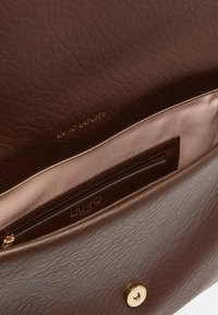 Intérieur d'un sac à main en cuir marron avec une finition texturée, présentant un revêtement beige, une poche zippée et des détails en logo et quincaillerie dorés.