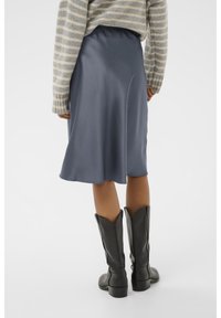 Jupe midi en satin bleu avec une taille élastique, associée à un pull rayé gris et des bottes noires jusqu'aux genoux. Texture lisse, design fluide.