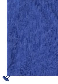 Tissu bleu texturé avec un petit cordon réglable à bouton-pression au bas sur fond blanc.