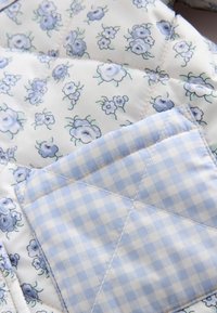 Gequilteter Stoff mit einem floralen Muster in Blau- und Weißtönen, der mit einem Gingham-Akzent in hellblau und weißen Karos verziert ist, mit gestickten Details.
