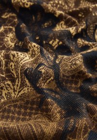 Brown fabric with intricate black and gold patterning, featuring textured ridges and smooth areas, creating a layered visual effect.