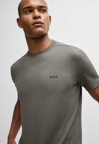 Kortermet grå T-skjorte laget av mykt stoff, med en ribbestrikket rund hals og en subtil svart "BOSS"-logo på brystet.