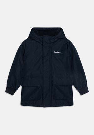 Veste imperméable bleu marine en tissu texturé, dotée d'une capuche, de deux poches avant et de poignets élastiques. Logo Timberland affiché.