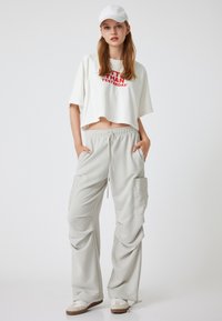 Afgemaakte witte T-shirt met rode tekst, gecombineerd met lichte grijze wijde cargo-broeken met zijzakken. Draag het met een witte pet en sneakers.