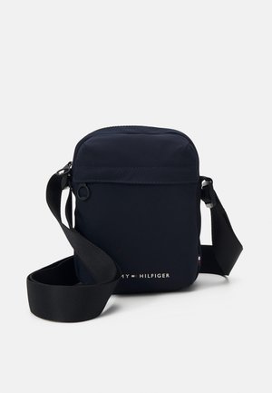 Borsa a tracolla in nylon navy con cintura regolabile, apertura con zip e tasca frontale. Presenta il logo del marchio in dettagli bianchi e rossi. Design compatto.
