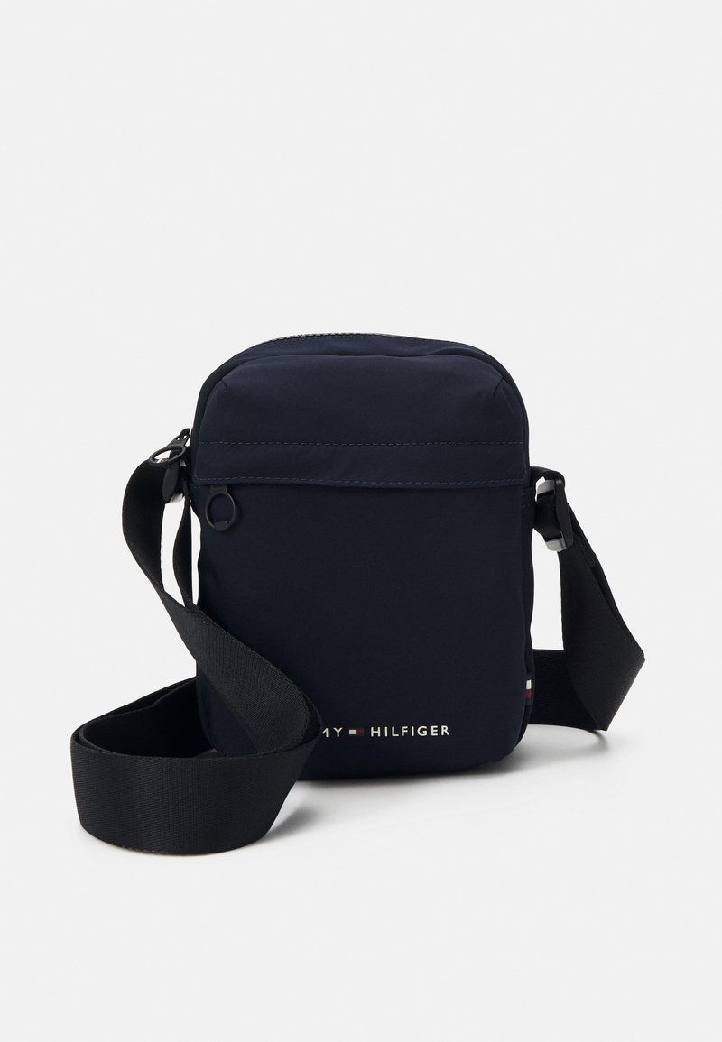 Borsa a tracolla in nylon navy con cintura regolabile, apertura con zip e tasca frontale. Presenta il logo del marchio in dettagli bianchi e rossi. Design compatto.
