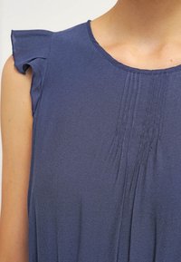 Blusa sin mangas de color azul marino con pequeños detalles fruncidos en los hombros, plisados en el escote y una textura de tela suave.