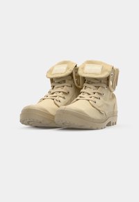 Bottines beige en toile avec un col rembourré, design à lacets, semelle en caoutchouc et un rabat pliable avec un logo.