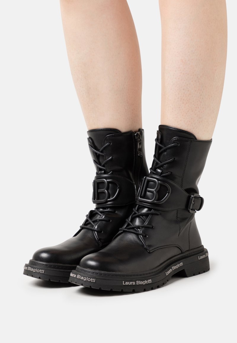 Botines de piel negra con cordones, cremallera lateral y una hebilla prominente con la letra "B". Suela texturizada con detalle de marca.