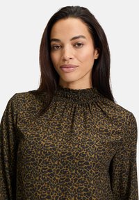 Blusa stampa leopardo realizzata in tessuto morbido, con scollo arricciato e maniche lunghe, nei colori marrone e nero.