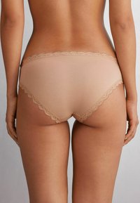 Beige panties met kantafwerking, featuring een gladde stof, een low-rise ontwerp, en een golfrand langs de tailleband en beenopeningen.
