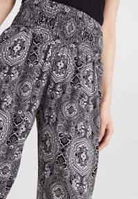 Black and white patterned pants with an elastic waistband, featuring a paisley design and soft fabric texture. Close-up of hand on garment.