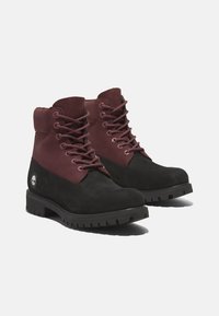 Bottines noires et bordeaux en daim et cuir, avec une semelle en caoutchouc robuste, un bout rond et un laçage sur le devant avec des œillets en métal.
