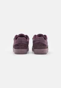 Sneakers viola con tomaia in suede e sintetico, collare imbottito, suola testurizzata e logo sul tallone. La vista posteriore mostra i dettagli del design.