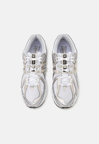 Scarpe sportive bianche con parte superiore in rete, dettagli in argento e nero, suola imbottita e lacci a contrasto; marchio presente sul lato esterno.