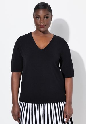 Maglione nero a maniche corte con scollatura a V, texture a coste e un discreto logo. Abbinato a una gonna a righe bianche e nere.