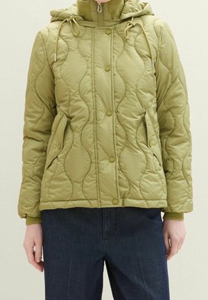 Veste matelassée vert olive avec boutons-pression à l'avant, fermeture éclair, deux poches à boutons-pression et une capuche ajustable portée avec un pantalon foncé.