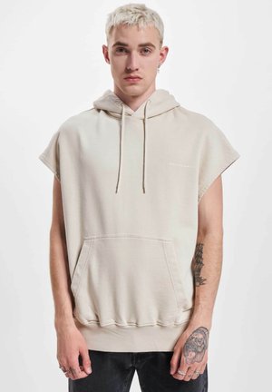 Beige ermeløs hettegenser laget av bomullsblanding, med kengurulomme, snorhette og ribbestrikket kant. Tekstlogo på brystet.