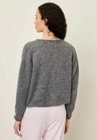 Šedý pletený svetr s uvolněným střihem, kulatým výstřihem a dlouhými rukávy, vyrobený z měkkého materiálu, s viditelnou texturou a jemnými detaily.
