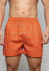 Shorts de bain orange avec un motif de grains de maïs soufflé. Ceinture élastique et coupe décontractée. Le matériau semble léger et doux au toucher.