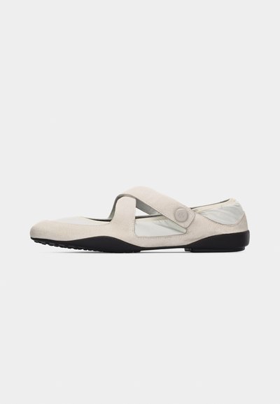 Beige Mary Jane shoe with crisscross strap, black sole, and soft fabric upper, designed for casual comfort and everyday wear.