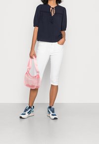Blusa navy con maniche a sbuffo corte e un fiocco al collo, abbinata a pantaloni capri bianchi. Una borsa rosa traslucida e sneakers multicolori completano il look.