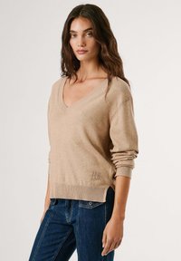 Bežna pletena majica z V-izrezom, dolgimi rokavi in ribastimi manšetami. Ima diskretno vezenje logotipa na robu, nosi se z modrimi kavbojkami.