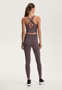 Fialový športový crop top so skríženými ramienkami a kruhovým výrezom. Skombinovaný s vysokými legínami a čiernymi teniskami.