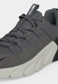 Σκούρο γκρι αθλητικό παπούτσι Nike Free με επάνω μέρος από διχτυωτό υλικό, παχιά λευκή σόλα με τμήματα και κορδόνια σε μορφή θηλειάς.