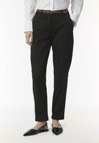 Zwarte op maat gemaakte broek met een slim fit, zijzakken en een soepele textuur, gecombineerd met een bruine leren riem en zwarte puntige ballerina's.