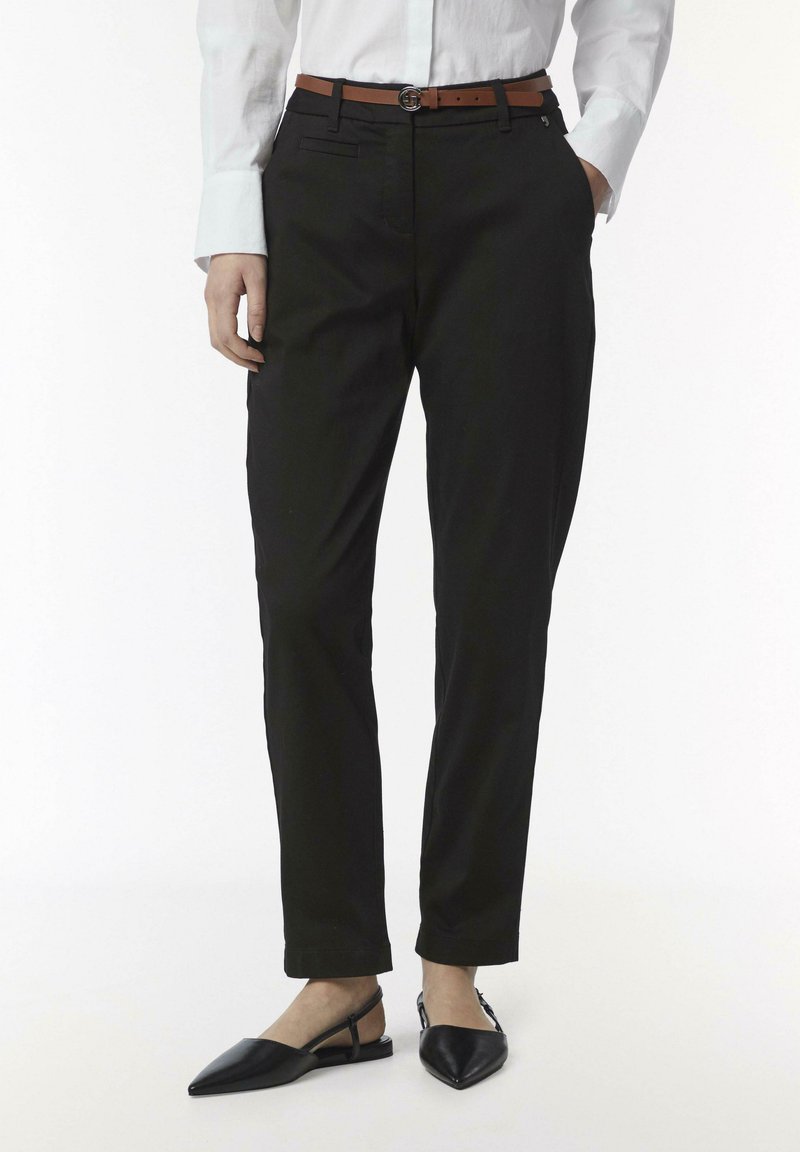 Zwarte op maat gemaakte broek met een slim fit, zijzakken en een soepele textuur, gecombineerd met een bruine leren riem en zwarte puntige ballerina's.