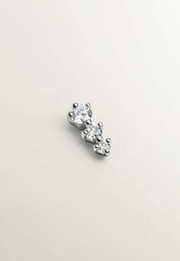 Tres gemas redondas y transparentes en un ajuste de plata con garras, dispuestas en un patrón de tamaño descendente, sobre un fondo neutro.