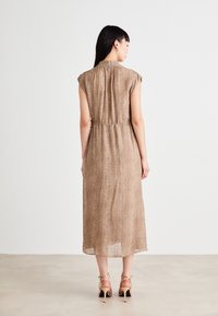 Rjava obleka do kolen s kratkimi rokavi, elastičnim pasom, teksturirano blago in diskretno vzorčno zasnovo. Nosi se z svetlimi petami.