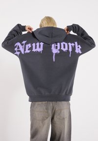 Dark grey hoodie featuring a purple dripping font text "New York" on the back. Designed with a kangaroo pocket and adjustable hood.
