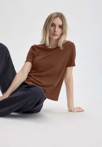 T-shirt marrone a maniche corte realizzato in tessuto morbido, con una vestibilità rilassata e un colletto girocollo classico, abbinato a pantaloni larghi blu navy.
