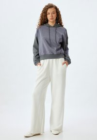 Sudadera corta gris y púrpura con un acabado texturizado y cordones, combinada con pantalones de pierna ancha en un suave tono crema. Ambos son casuales y suaves.