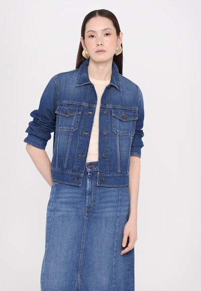 Denim jacket in dark blue with two chest pockets, button closure, and rolled-up sleeves, paired with a matching blue denim skirt.
